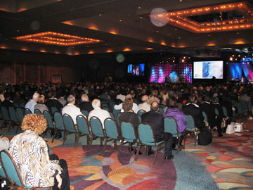 Audience facing video screens in a banquet hall, with circular light spots (angel orbs) in the photograph