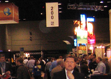 Convention visitors beneath a hanging aisle sign, with a circular light spot (angel orbs) near the ceiling