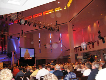 Side view of an auditorium audience and stage, with circular light spots (angel orbs) in the photograph