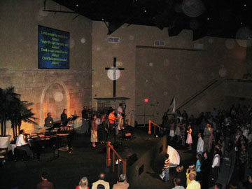 Congregation facing a cross and projected words, with circular light spots (angel orbs) in the photograph