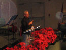Speaker at a lectern beside red flowers, with circular spots visible nearby