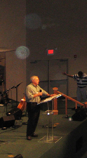 Man playing guitar beside a lectern, with circular light spots (angel orbs) in the photograph