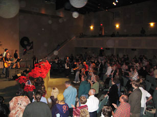 Standing auditorium audience beside red flowers, with circular light spots (angel orbs) in the photograph