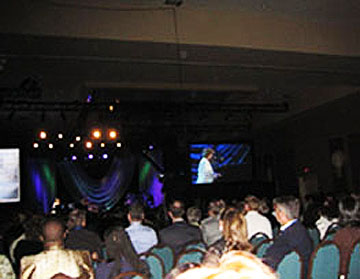 Audience facing a dark stage with video screens