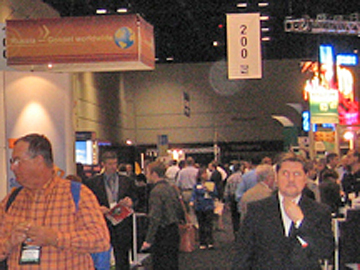 People at a convention hall with hanging signs and a pale circular spot (angel orbs) near the ceiling