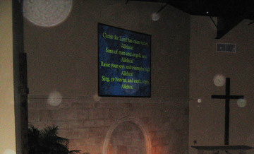 Church wall with a cross and projected text, with circular light spots (angel orbs) visible