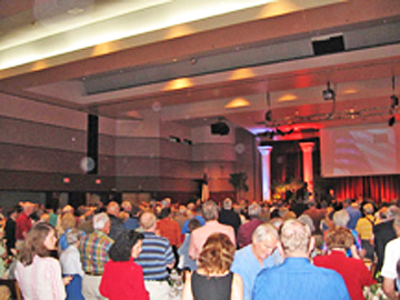 Crowded indoor banquet hall with circular light spots (angel orbs) visible above the audience