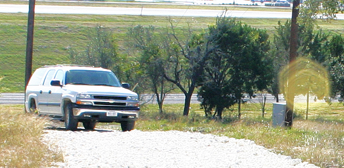 White vehicle on a gravel drive with a yellow circular flare at the right