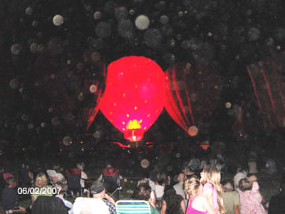 Glowing red hot-air balloon at a nighttime gathering with circular light spots (angel orbs) overhead