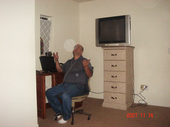 Man sitting beside a television and chest of drawers