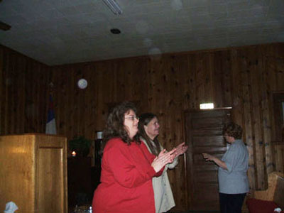 People standing inside a wood-paneled church, with pale circular spots (angel orbs) near the ceiling