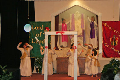 People performing on a church stage with a bright circular light spot (angel orbs) beside them