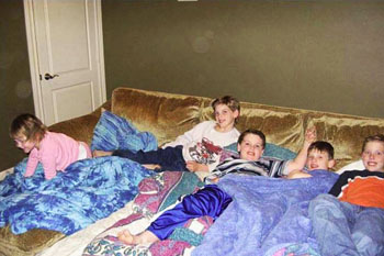 Children resting together beneath blankets on a sofa