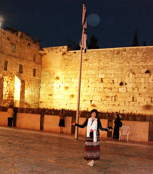 Person beside an Israeli flag at the Western Wall at night, with a circular light spot (angel orbs) above
