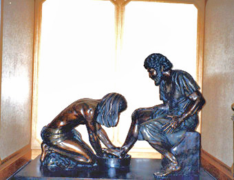 Divine Servant® bronze sculpture of Jesus washing Peter's feet, displayed indoors