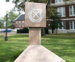 Stone pedestal with a carved cross emblem on the campus lawn