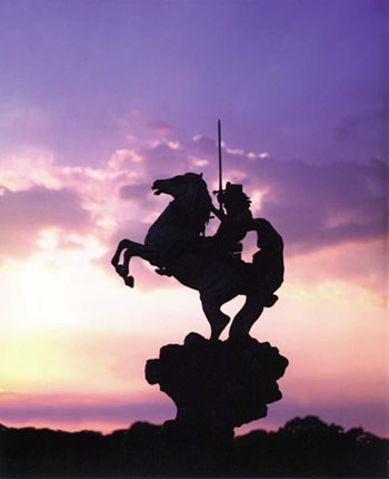 The Coming King® silhouetted against a purple and pink sunset