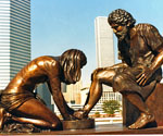Divine Servant® sculpture outdoors with city skyscrapers behind it