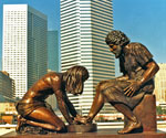 Divine Servant® sculpture outdoors with city skyscrapers behind it