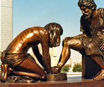 Divine Servant® sculpture outdoors with city skyscrapers behind it