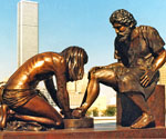 Divine Servant® sculpture outdoors with city buildings behind it
