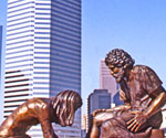 Divine Servant® sculpture outdoors with city buildings behind it