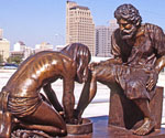 Divine Servant® sculpture outdoors with city buildings behind it