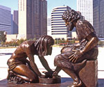 Divine Servant® sculpture outdoors with city buildings behind it