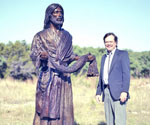 Man standing beside the life-size Fisher of Men® sculpture outdoors