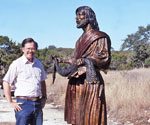 Man standing beside the life-size Fisher of Men® sculpture outdoors