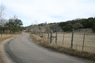 Paved road curving beside a fence through ranchland
