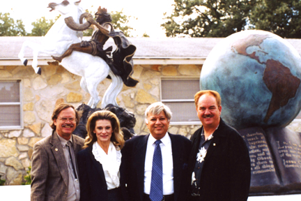 Four people posing before a sculpture display with a globe and mounted rider