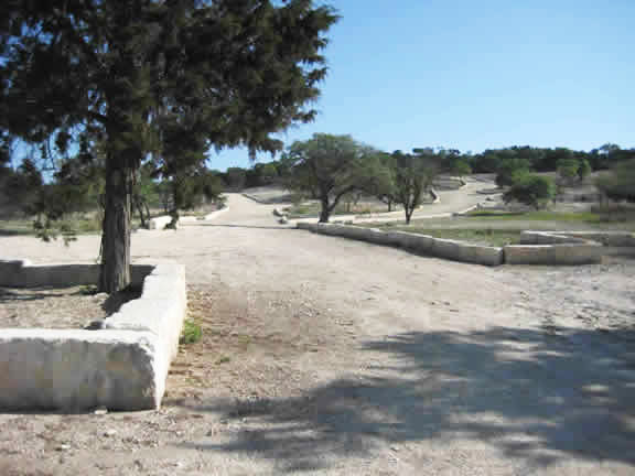Gravel ranch path between low stone walls and trees