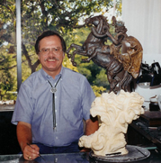 Artist beside a small horse-and-rider model with the larger sculpture behind