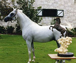 White horse posed beside a small mounted-rider sculpture outdoors