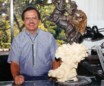 Artist beside a small mounted-rider model and an earlier finished sculpture