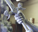 Side detail of the sword-gripping hand and sculpted sleeve