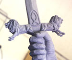 Sword crossguard and clenched hand against a light workshop background