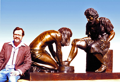 Artist seated beside the finished Divine Servant® bronze sculpture