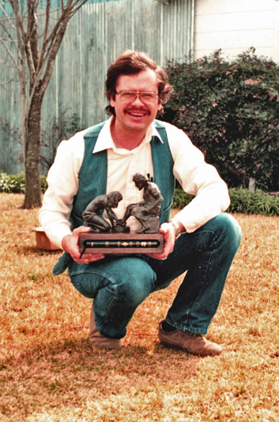 Max Greiner kneeling outdoors holding the small Divine Servant® sculpture