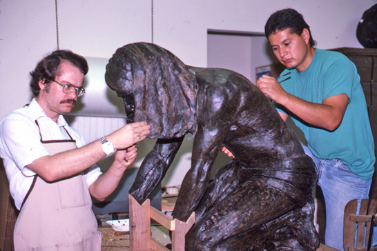 Two sculptors applying wax to the kneeling figure