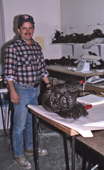 Foundry worker beside a detached wax sculpture section on a table