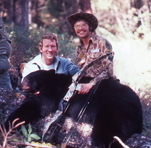 Two men posing with a harvested black bear and archery equipment